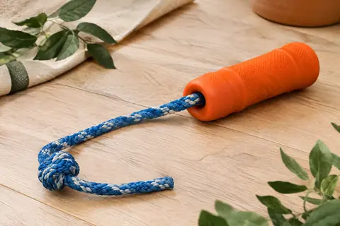 Jouet orange pour chien avec bumper en caoutchouc et corde déroulée, posé sur un sol en bois clair.