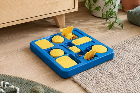 Planche puzzle pour chien bleue et jaune avec cases coulissantes et couvercles, posée dans un intérieur clair.