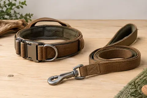 Collier tactique marron en nylon rembourré avec poignée, boucle métallique et laisse posés sur du bois clair.