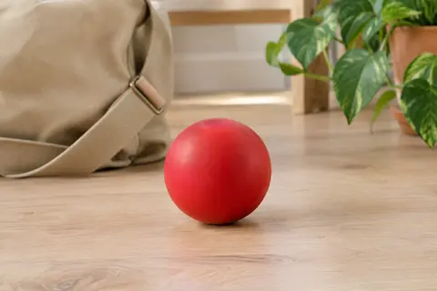 Balle ronde rouge en caoutchouc naturel posée sur un sol en bois clair