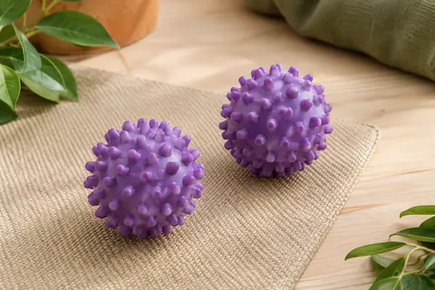 Deux balles violettes pour chien à picots, posées sur une toile sable dans un décor naturel lumineux.